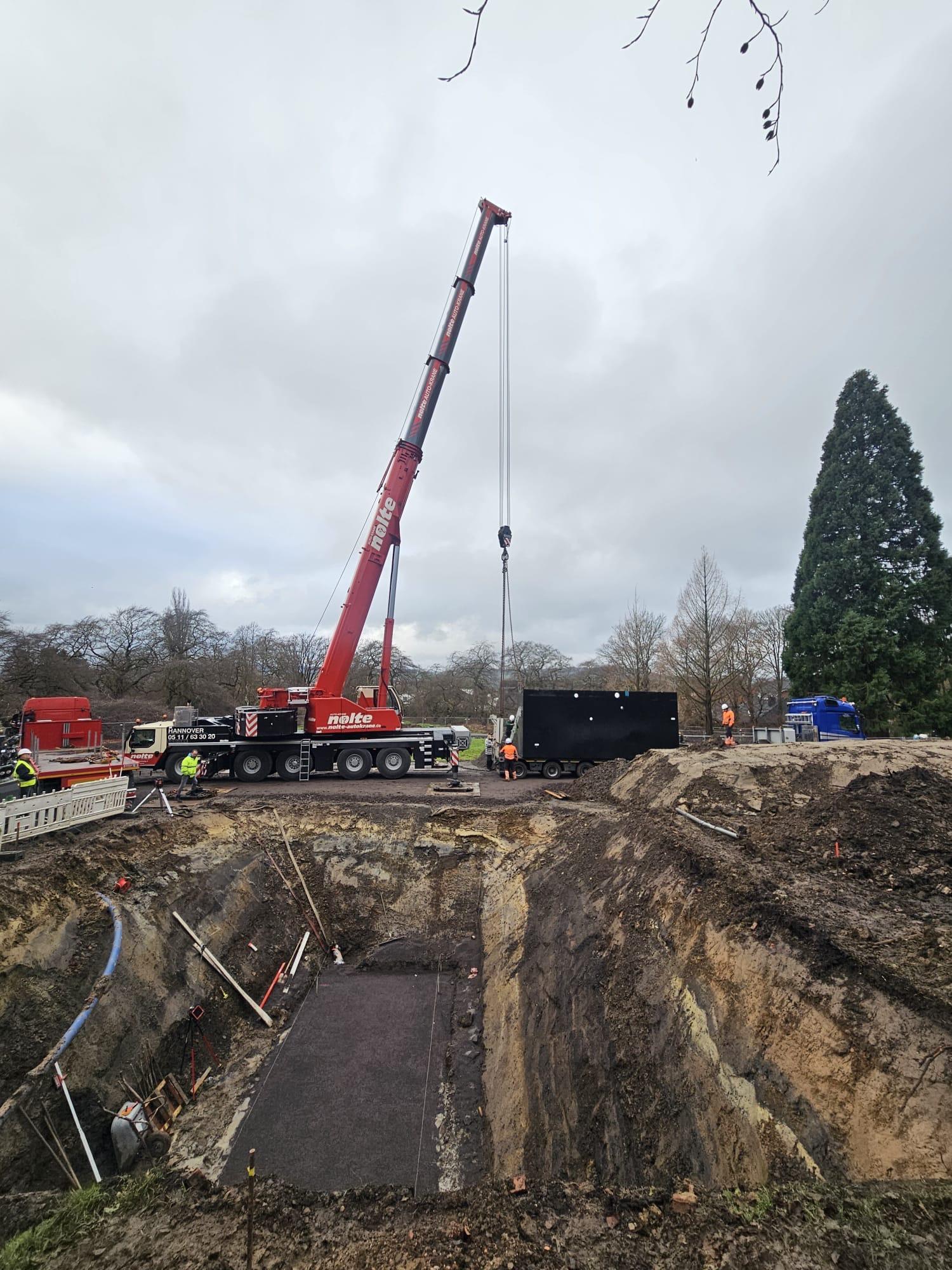 Der Autokran setzt das große Bauteil in die vorbereitete Grube.